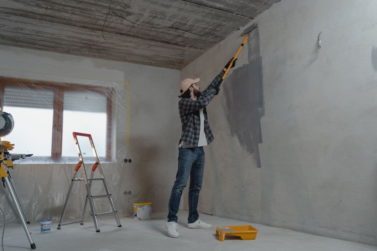 Contractor painting an interior wall with a roller on an extension pole